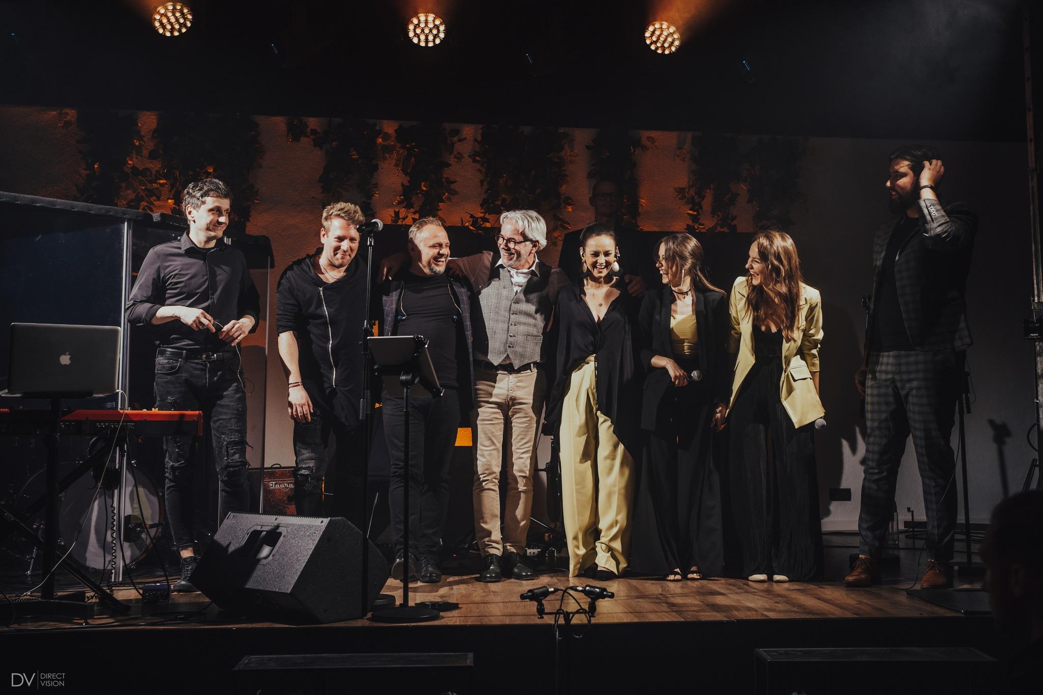 Artists and musicians stand together on stage after a performance during an anniversary concert.